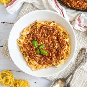 A white bowl of tagliatelle pasta topped with tofu mince in bolognese sauce.