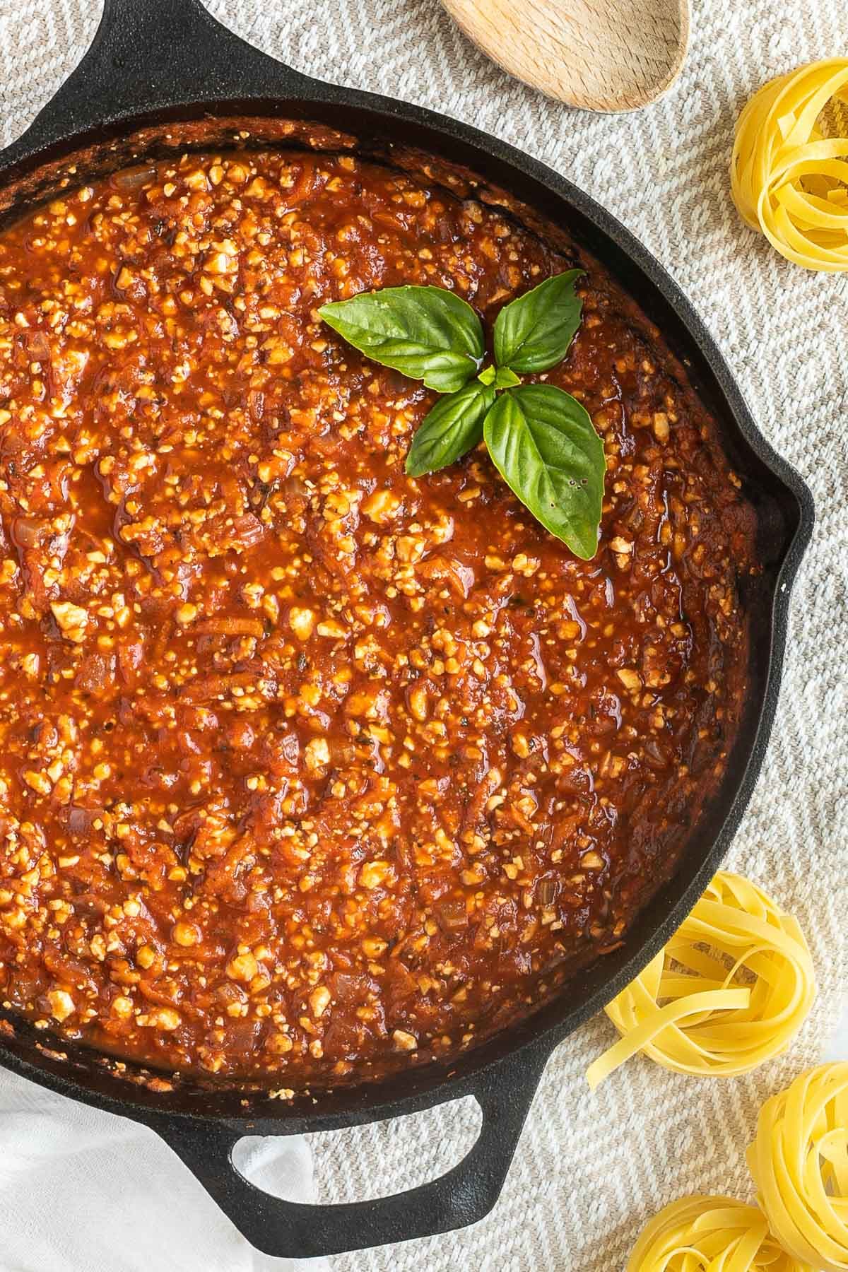 A cast iron skillet with tofu mince in bolognese sauce.