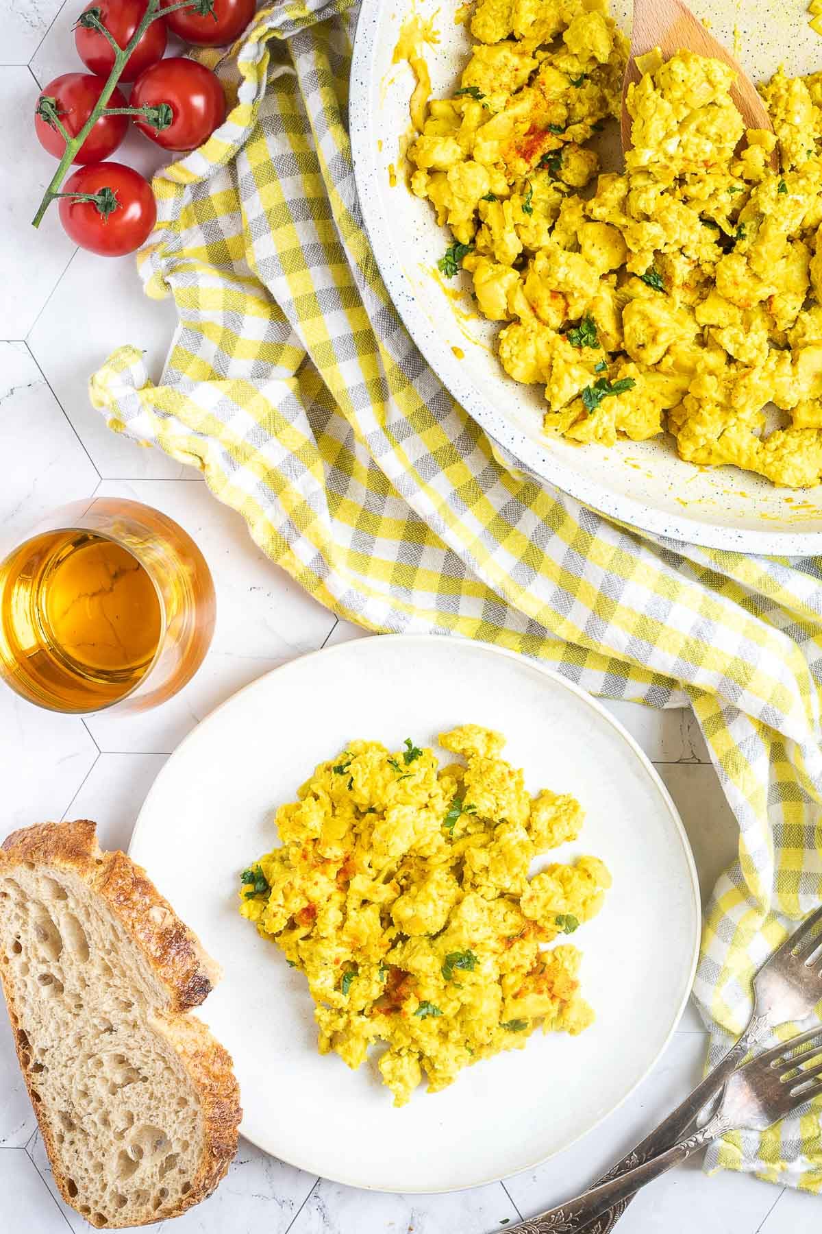 Vibrant yellow scrambled tofu is served on a small white plate. Leftovers are in a white frying pan next to it. 