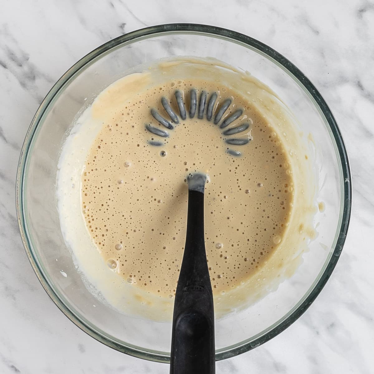 A glass bowl with light brown batter. A spatula is placed in the middle.