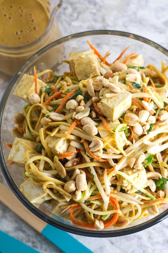 A glass salad bowl with sprouts, noodles, tofu cubes, and matchstick carrot.