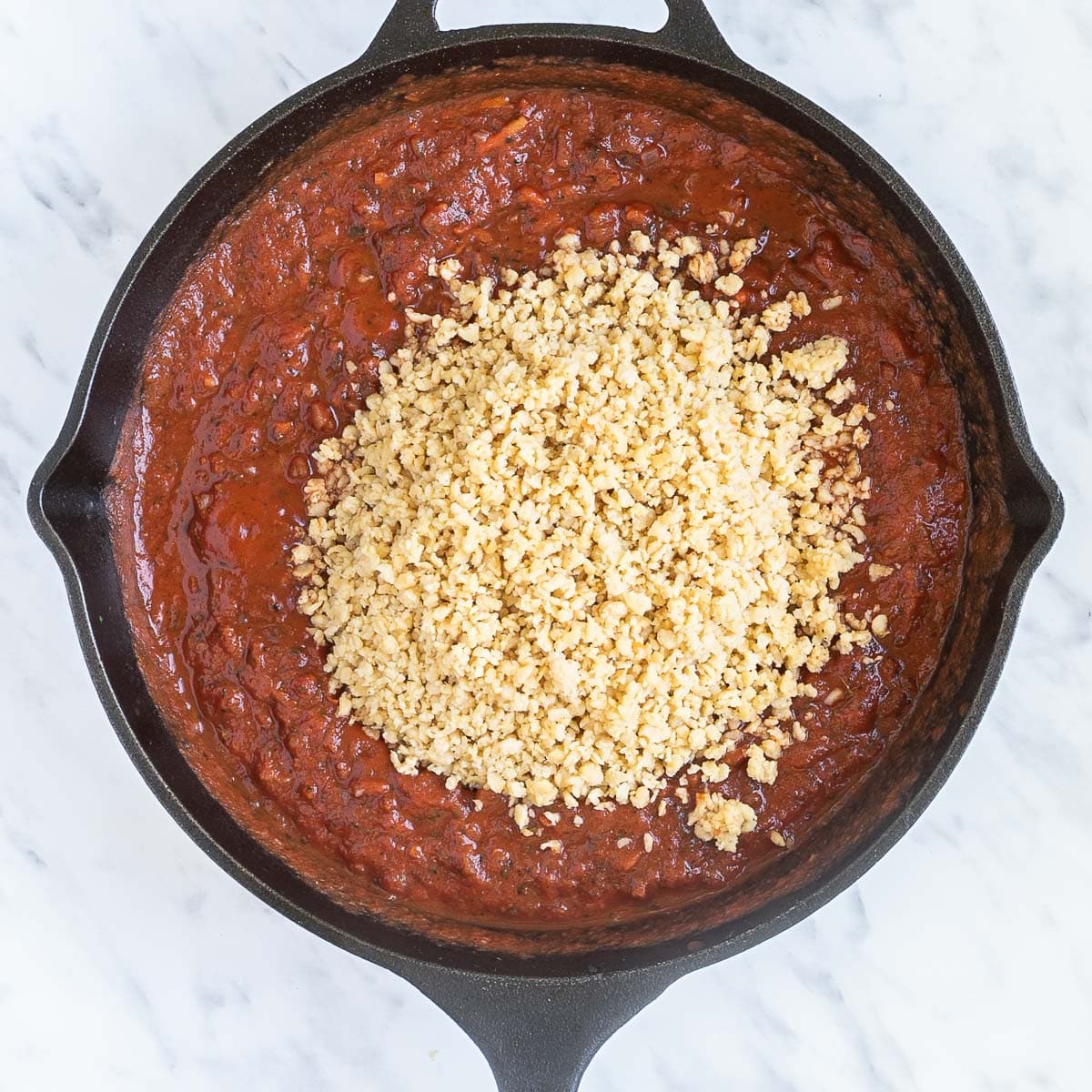 Red chunky sauce with meat-like crumbles on top in a cast iron skillet