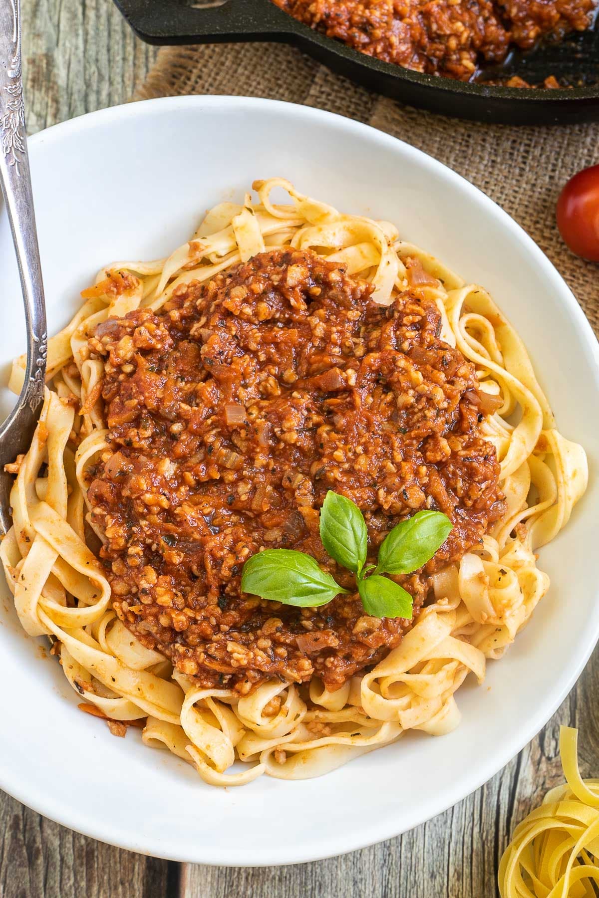 A white bowl of tagliatelle pasta topped with meat-like crumbles in bolognese sauce.