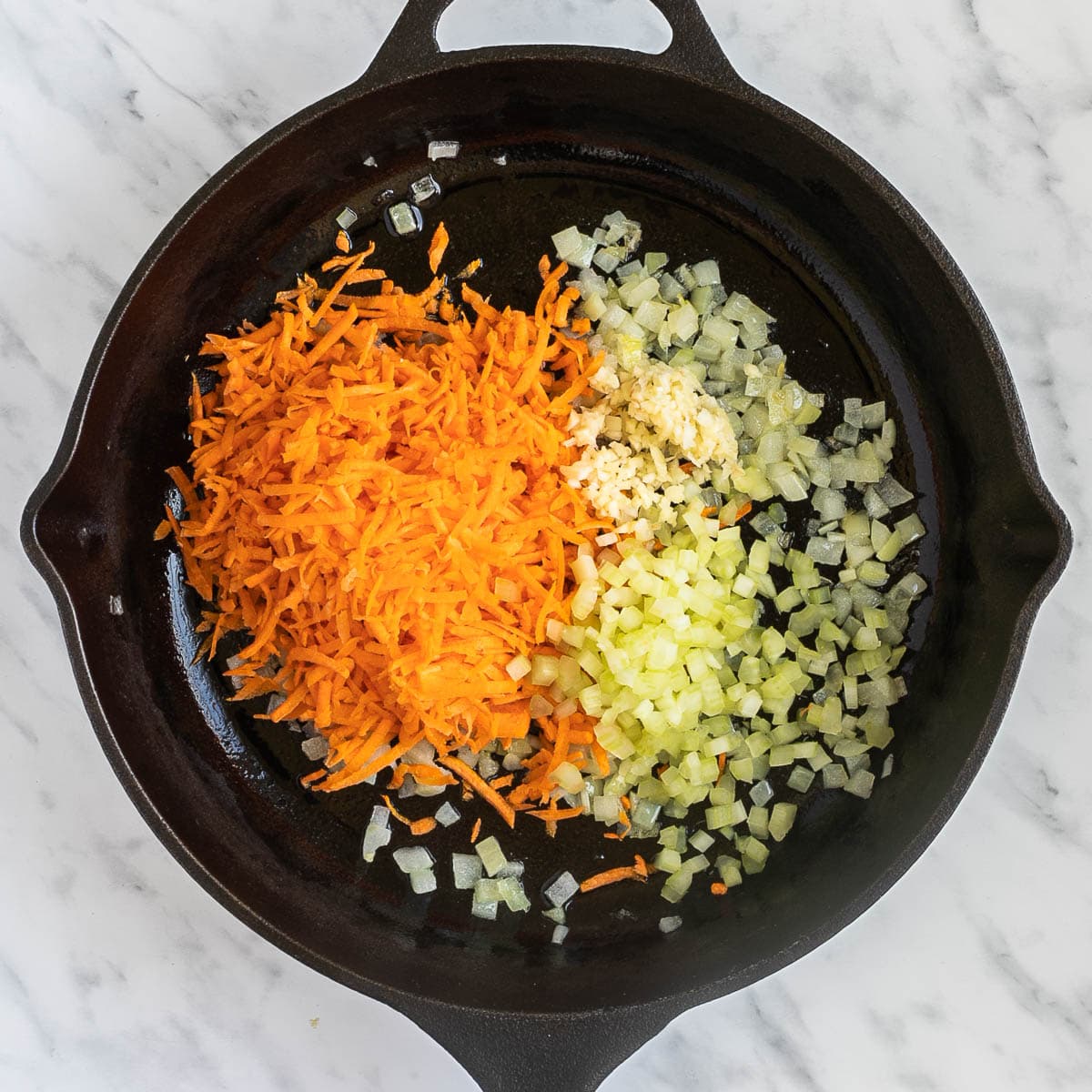 Cast iron skillet with heaps of finely chopped carrots, onion, garlic, and celery