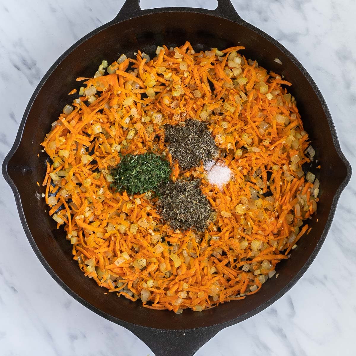 Cast iron skillet with a mix of finely chopped carrots, onion, garlic, celery, and heaps of spices in the middle.