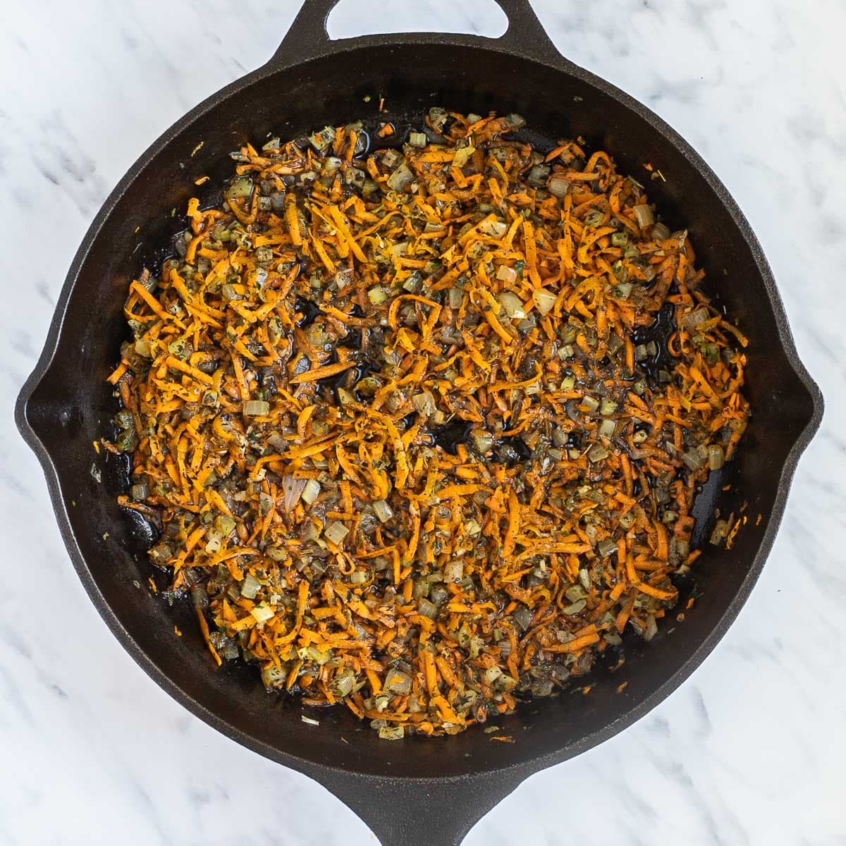 Cast iron skillet with a mix of sauteed finely chopped carrots, onion, garlic, and celery.