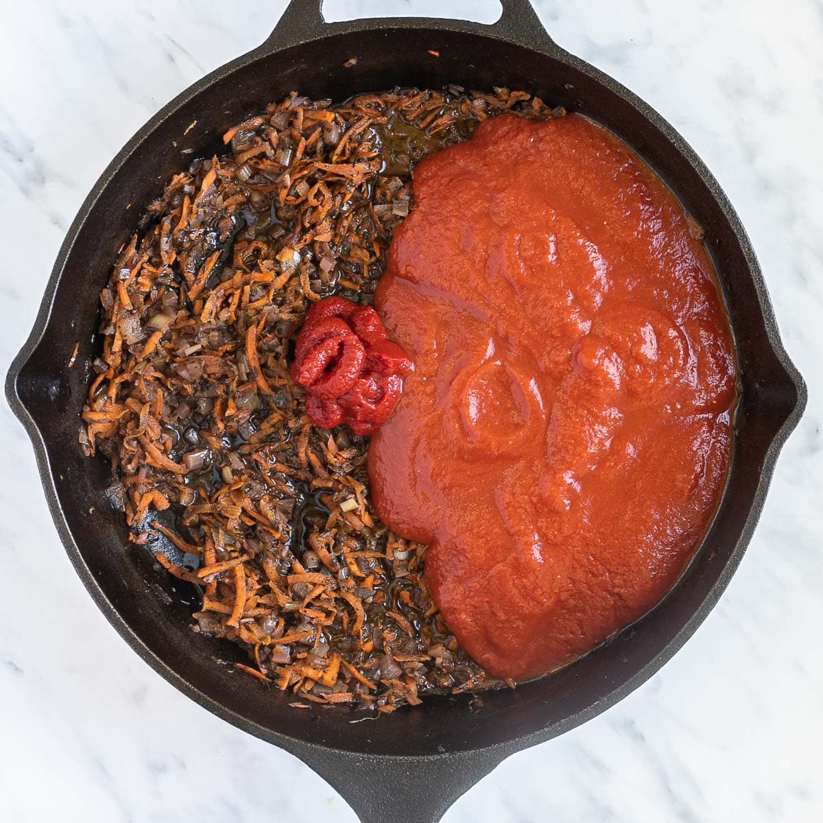 Cast iron skillet with a mix of brown sauteed finely chopped carrots, onion, garlic, celery and tomato sauce.