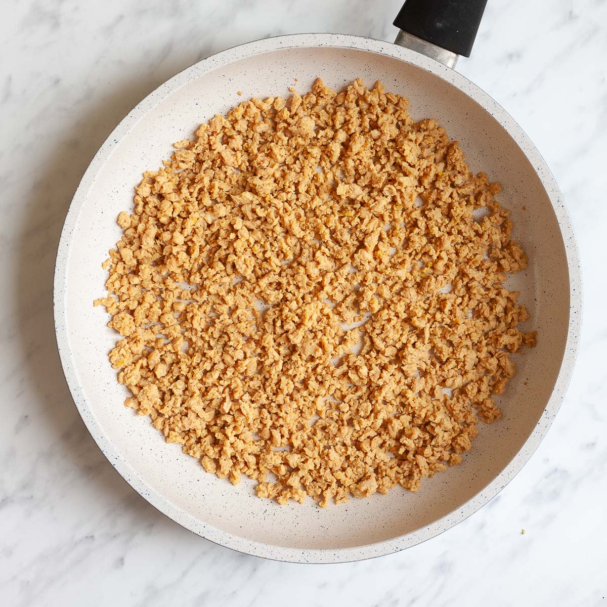 White frying pan with light brown crumbles that reminds you of ground beef