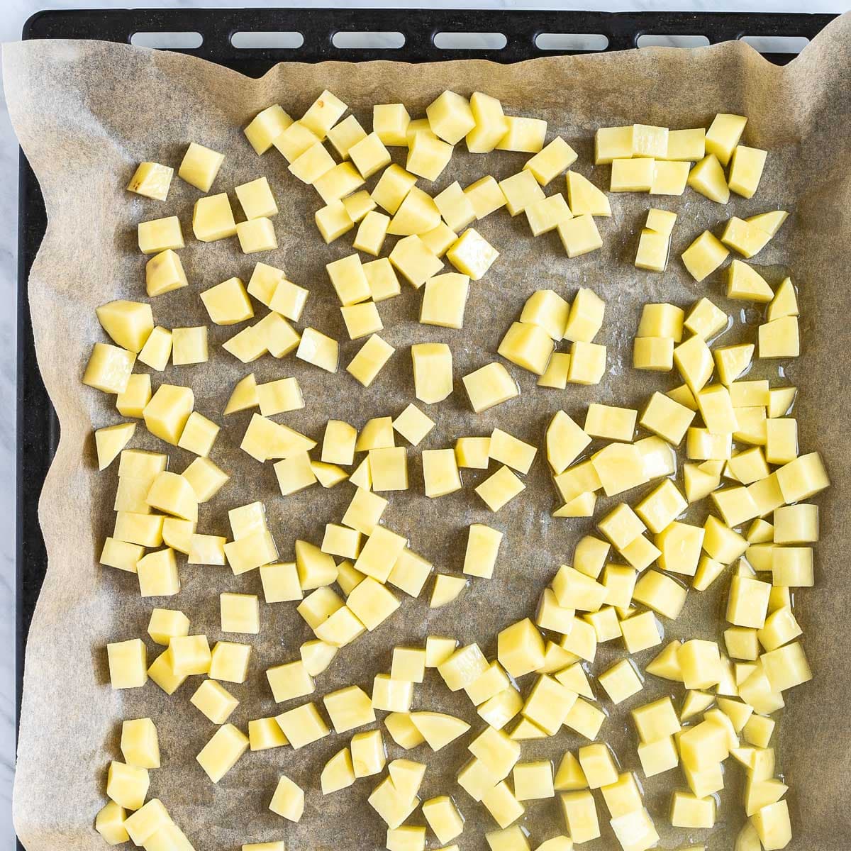 Sheet pan with yellow, raw, diced potatoes.