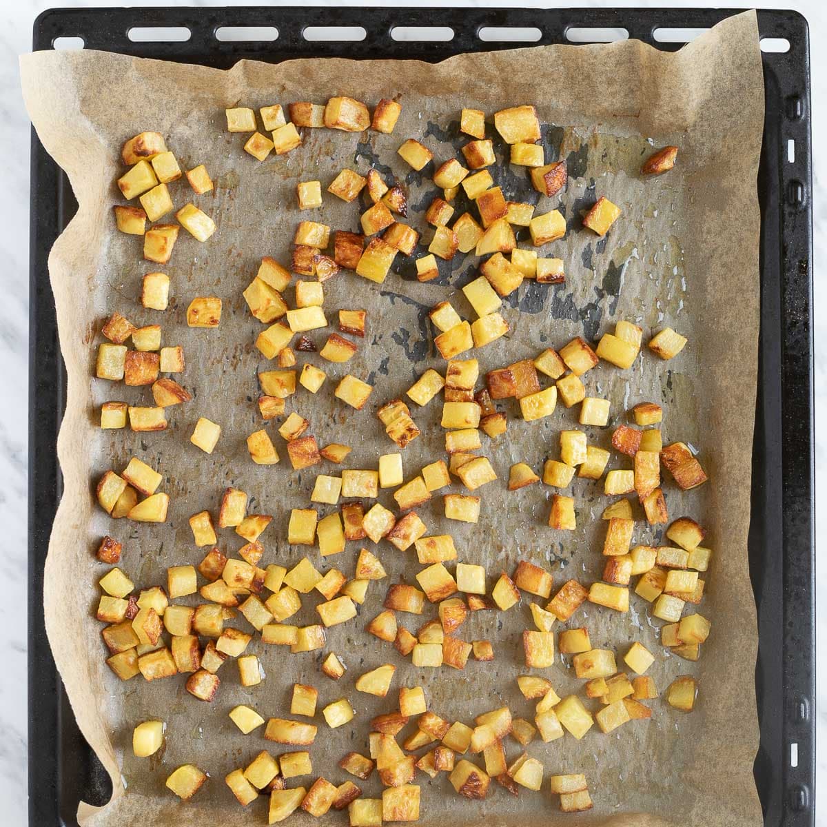 Sheet pan with crispy, brown, diced potatoes.