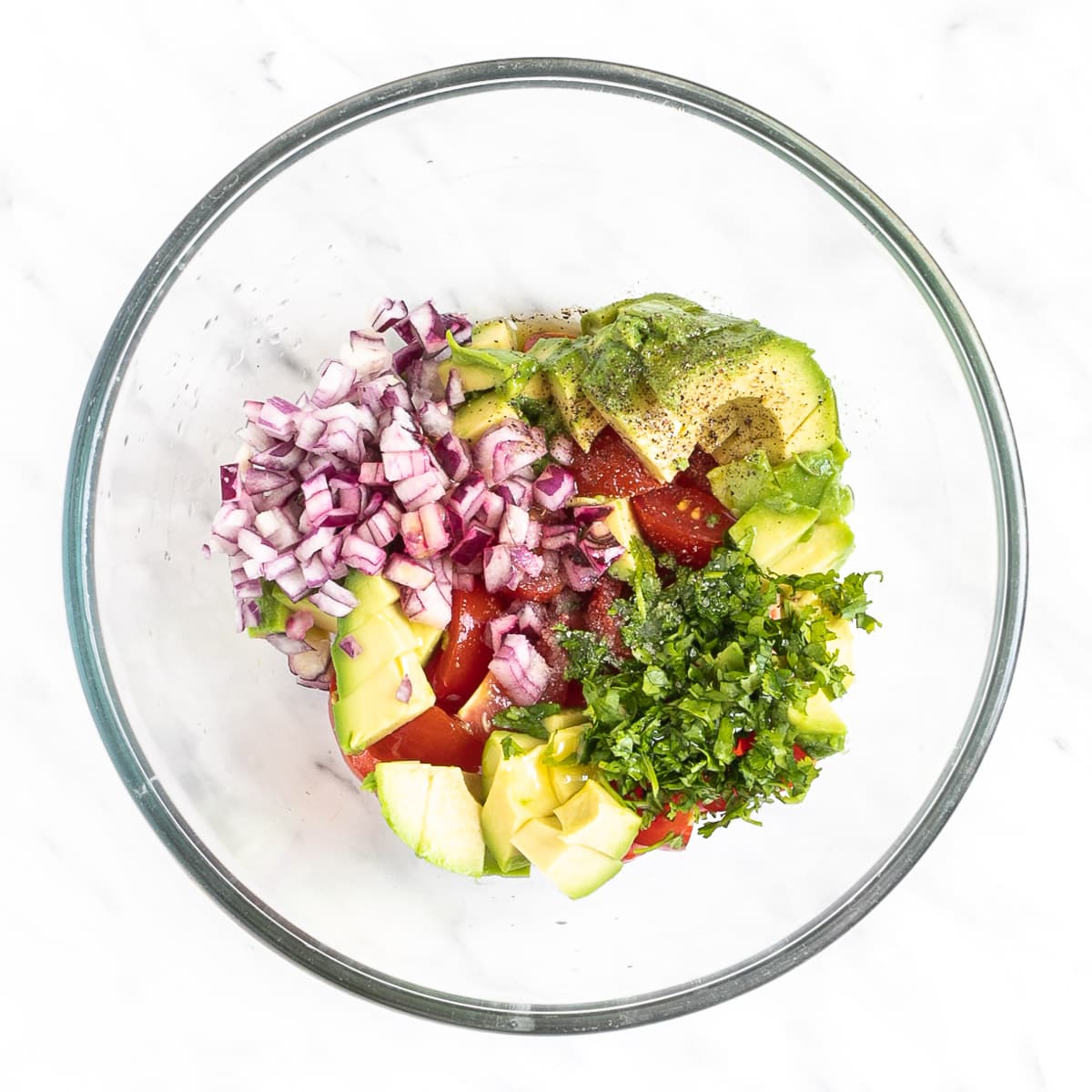 Glass bowl with avocado, cherry tomatoes, cilantro, chopped red onion.