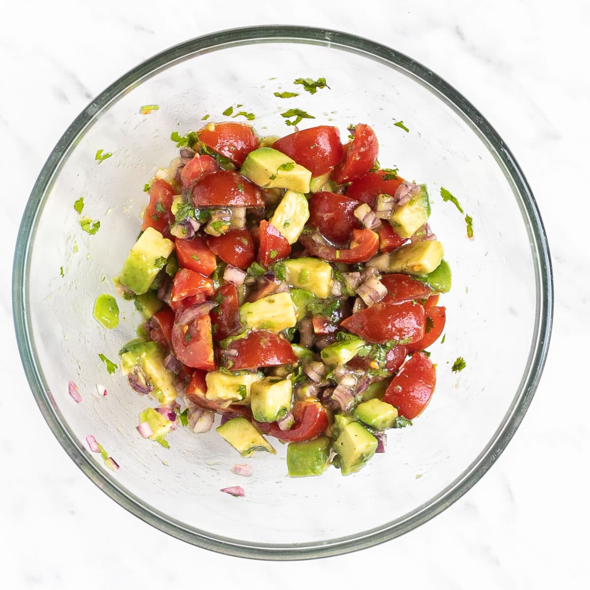 Glass bowl with a mix of chopped avocado, cherry tomatoes, cilantro, chopped red onion.