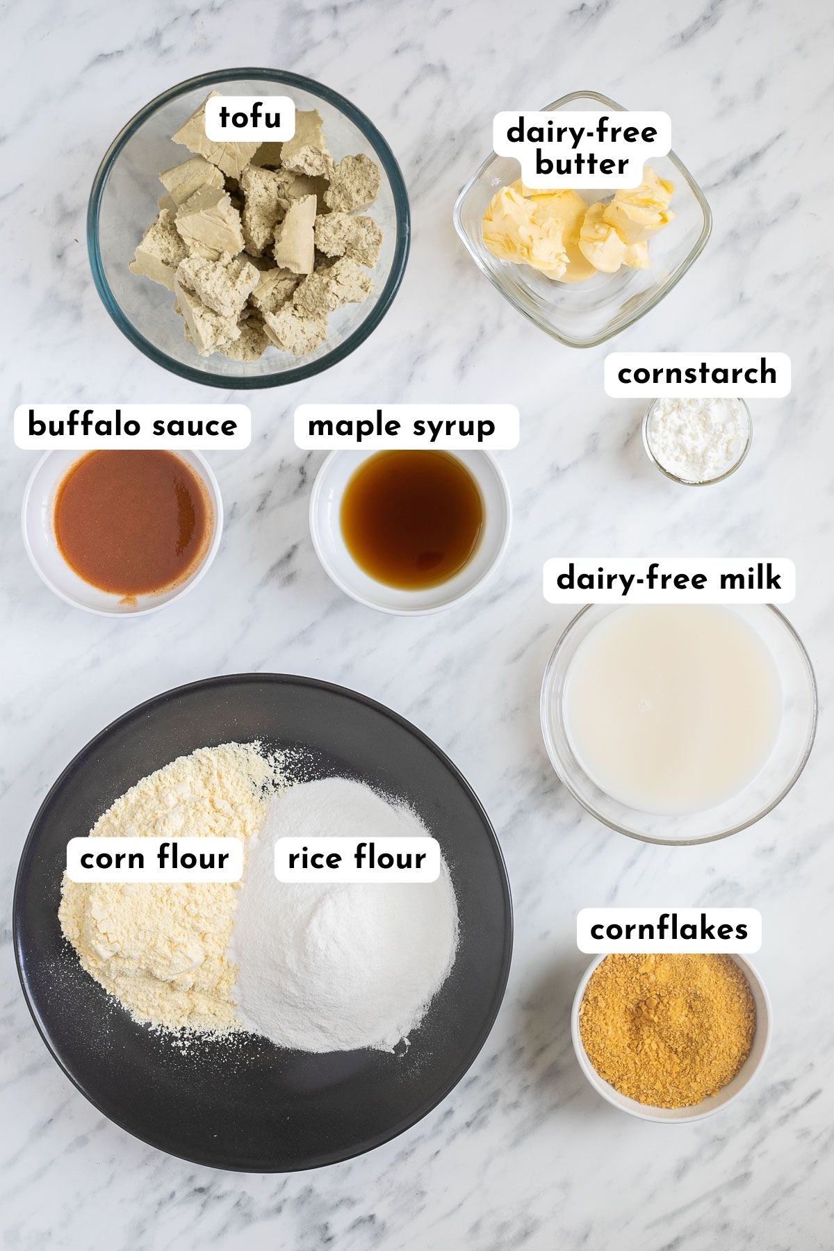 Ingredients of buffalo tofu in different plates and bowls like torn tofu, butter, red sauce, maple syrup, flours, milk, corn flakes.