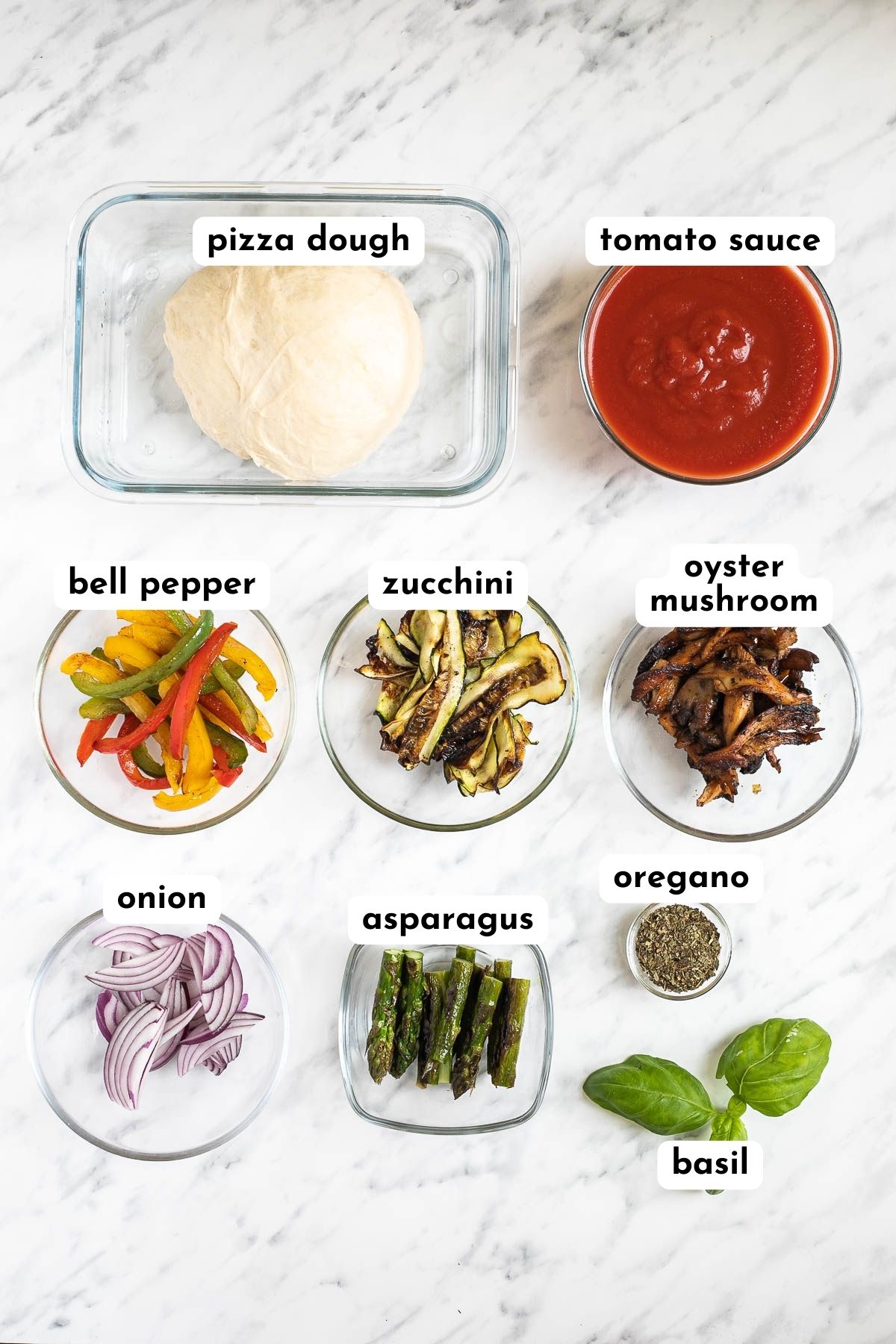Ingredients of cheeseless pizza in small containers like pizza dough, tomato sauce, bell pepper strips, zucchini, mushrooms, asparagus, red onion, basil and dried oregano
