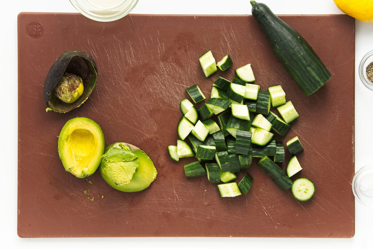 Peeled avocado and chopped cucumber on brown cutting board