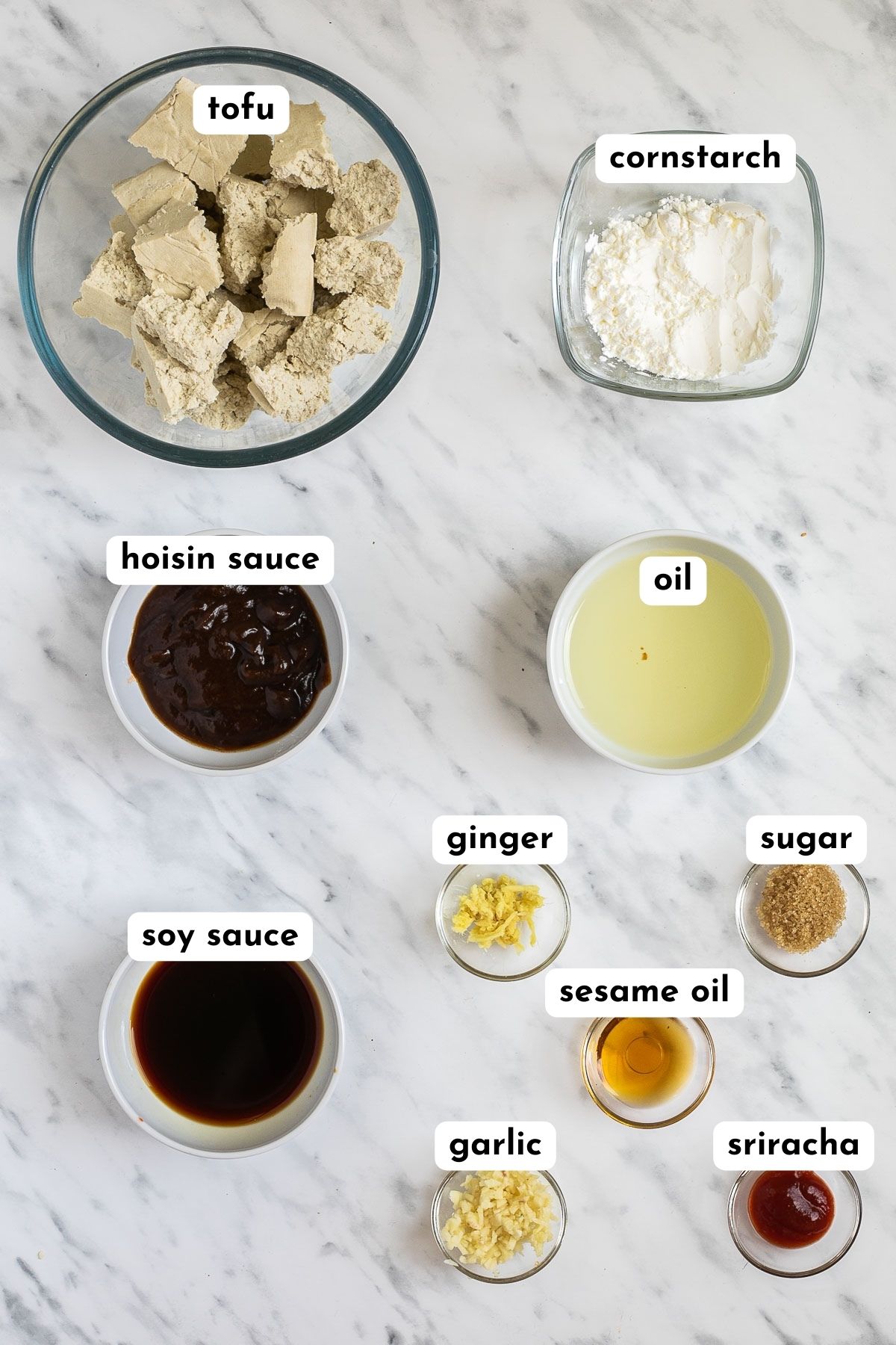 The ingredients of hoisin tofu in small glass bowls like oil, soy sauce, hoisin sauce, grated ginger, sugar, starch and torn tofu pieces