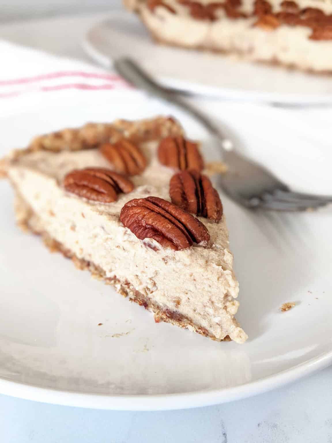 White plate with a slice of pie on it with pecans on top and a fork next to it.