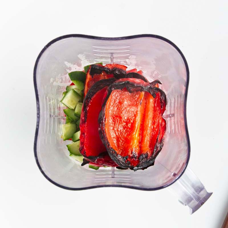 Blender with roasted red peppers on top of chopped veggies
