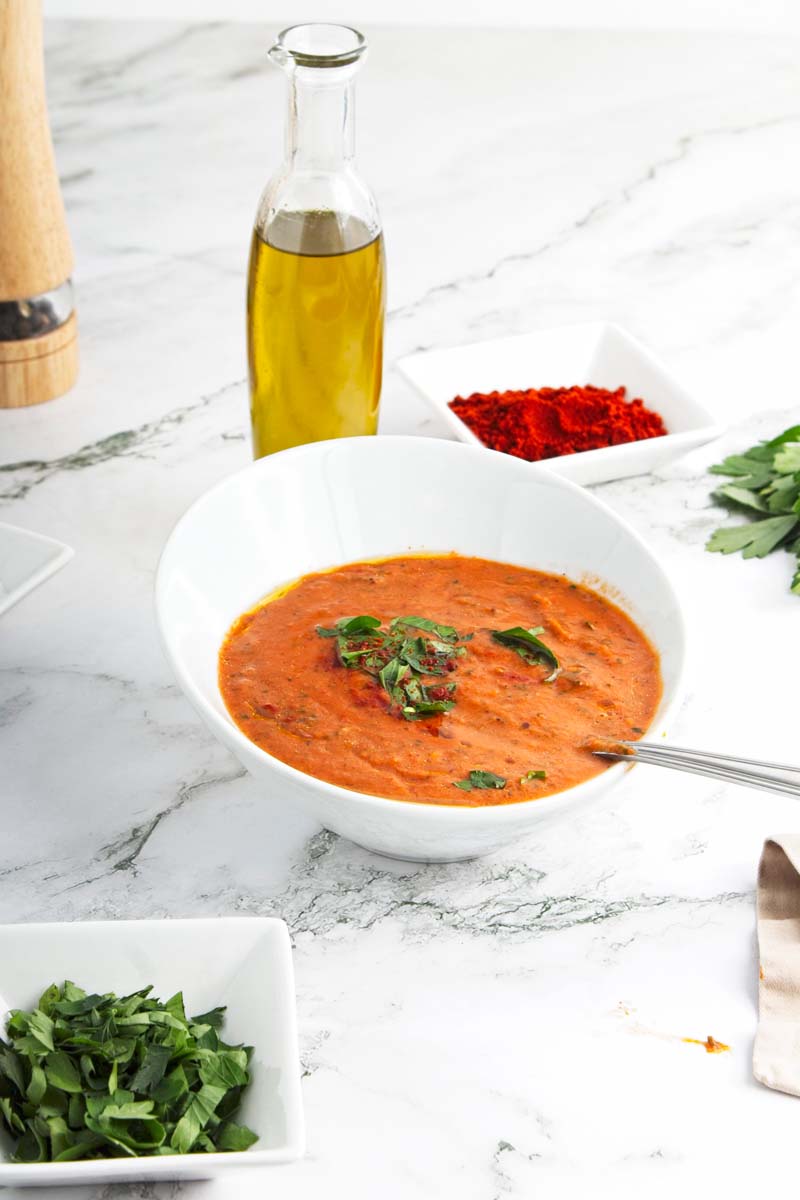 Red soup topped with chopped basil in a white bowl.