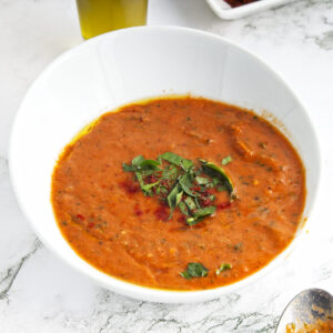 Red soup topped with chopped basil in a white bowl.