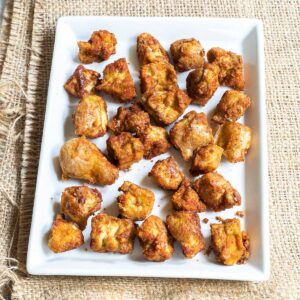 Baked, redish brown tofu pieces on white square plate.