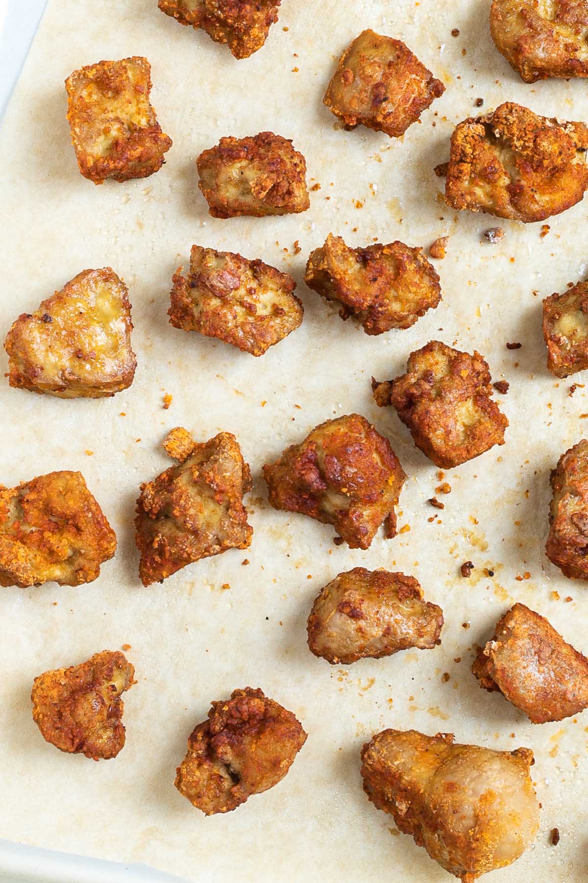 Baked, redish brown tofu pieces on a parchment paper.