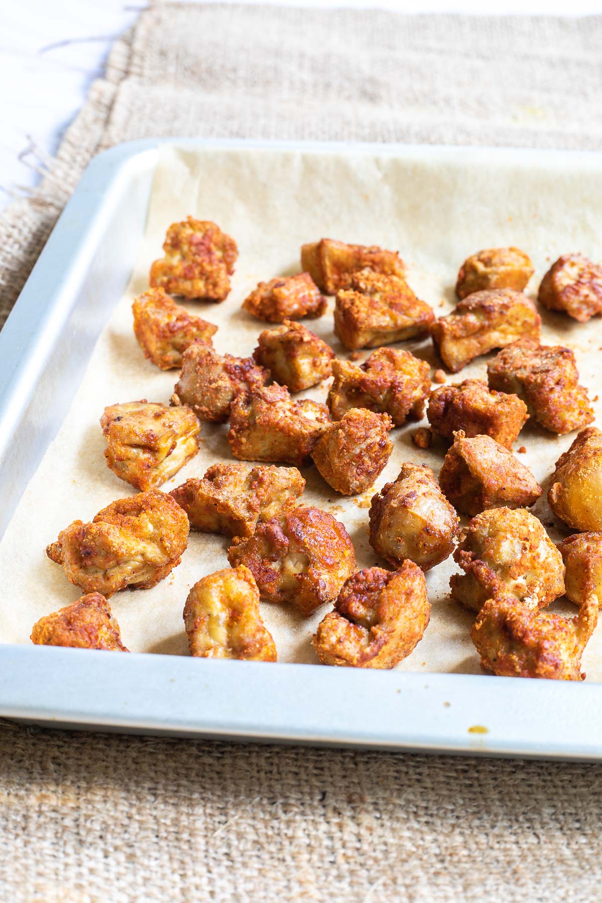 Baked, redish brown tofu pieces on a parchment paper in a silver baking tray.
