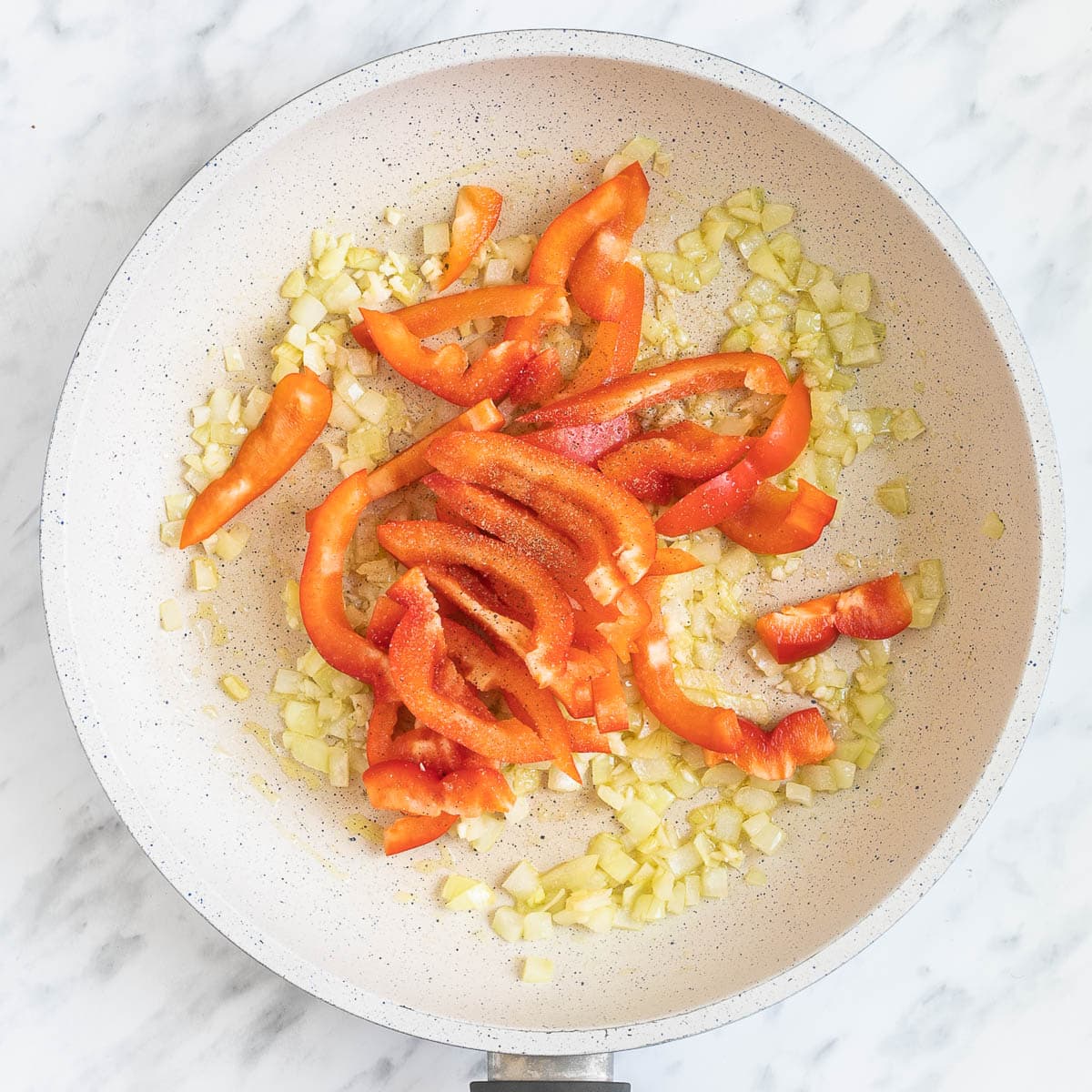 A white frying pan with chopped onions and red pepper slices