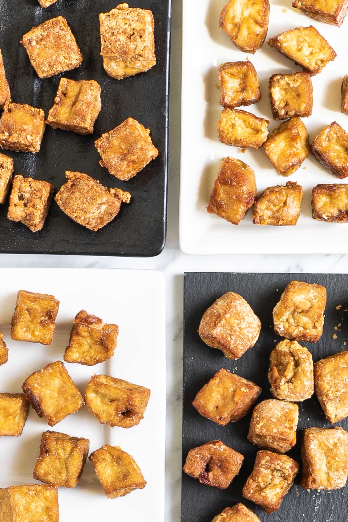 Crispy brown tofu cubes on 4 different plates of white and black.