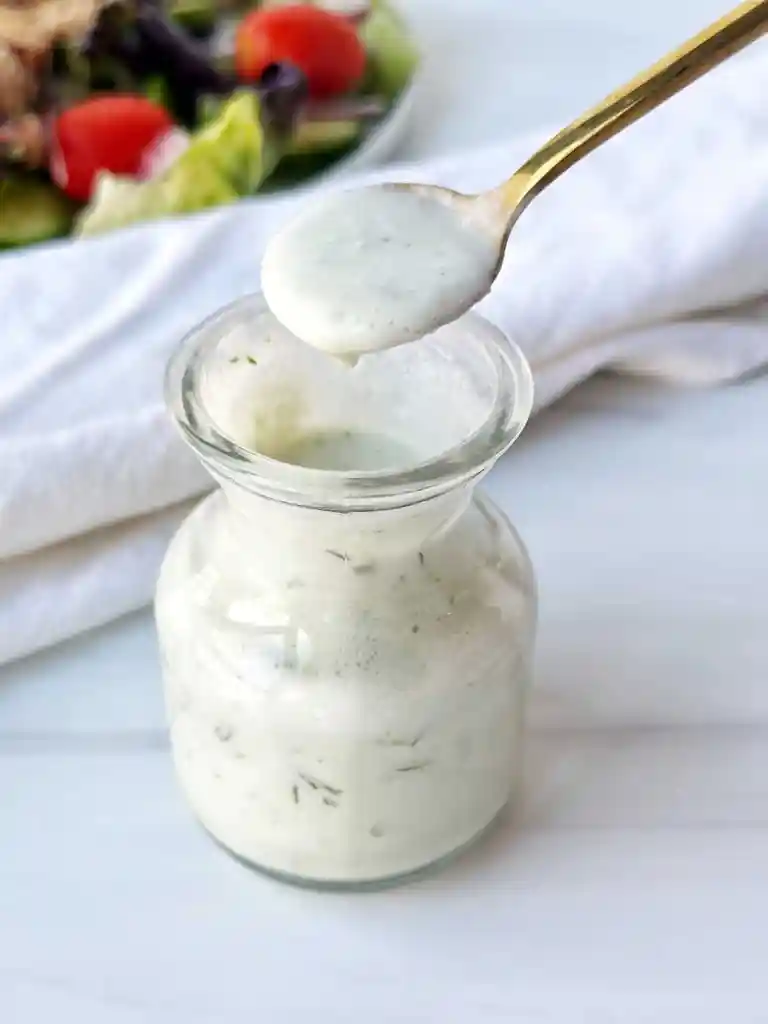 A jar of ranch sauce on a white table.