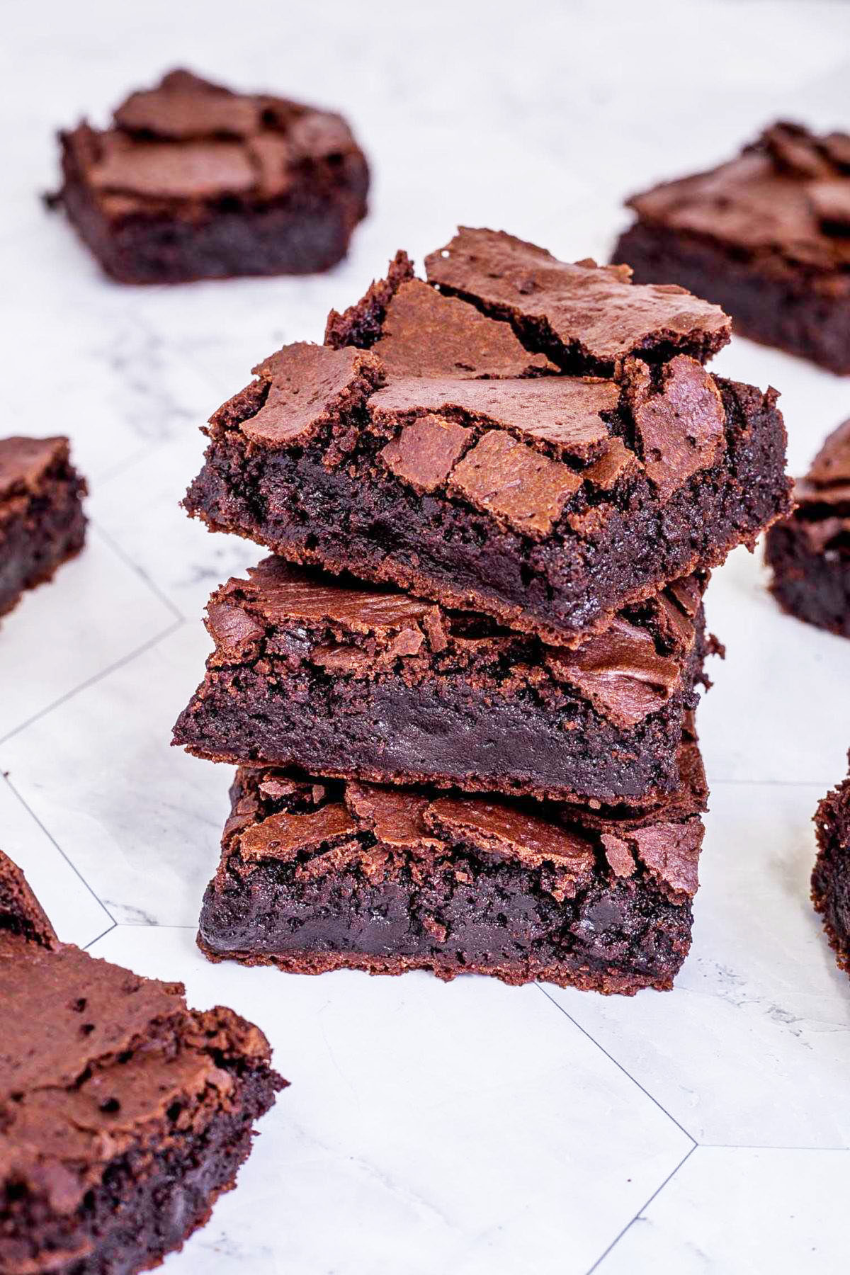 3 square brownies on top of each other with fudgy middle and crackly top. Several more scattered around. 