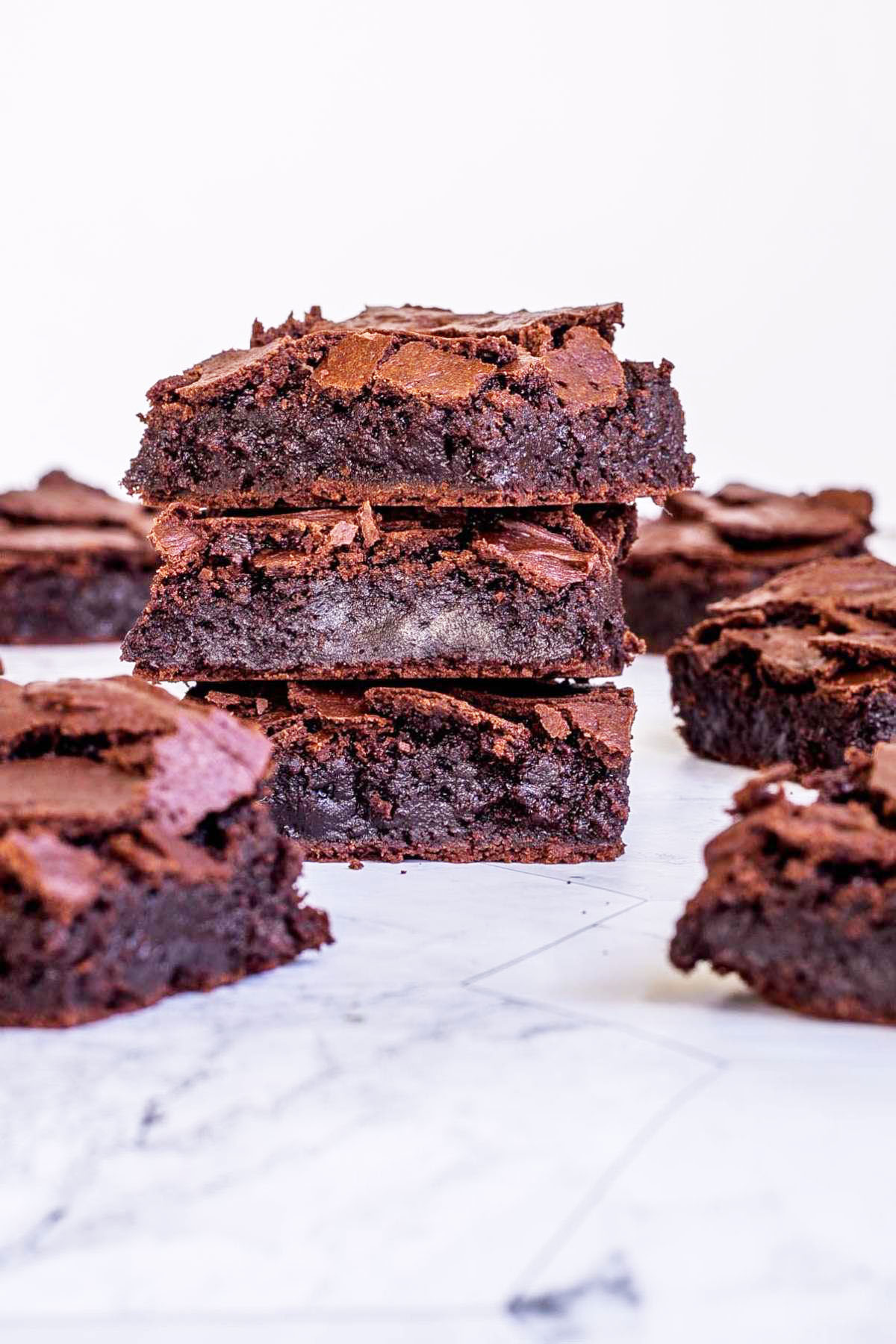 3 square brownies on top of each other with fudgy middle and crackly top. Several more scattered around.