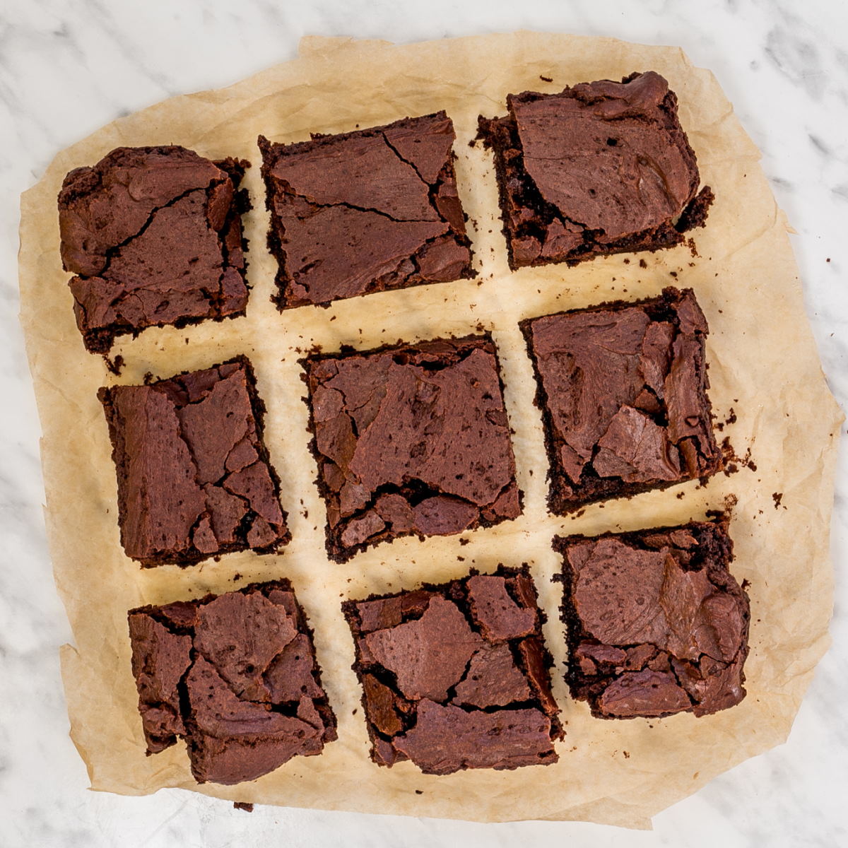 9 squares of brownies with crackly top on light brown parchment paper.