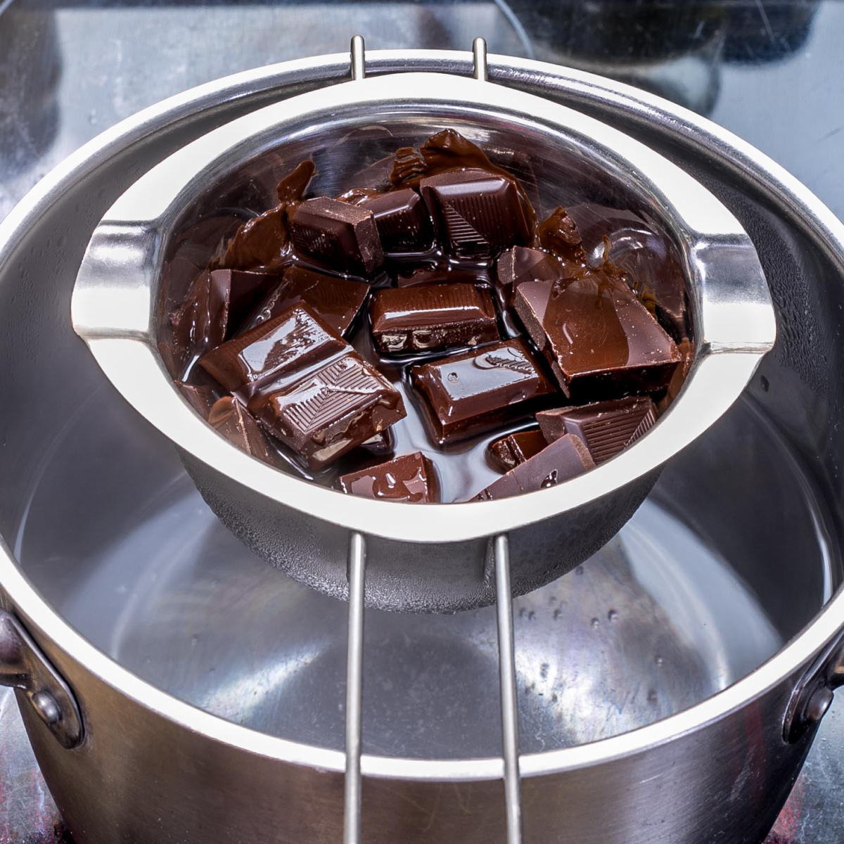 A small pot full of chocolate cubes and oil over a larger stockpot with boiling water. 