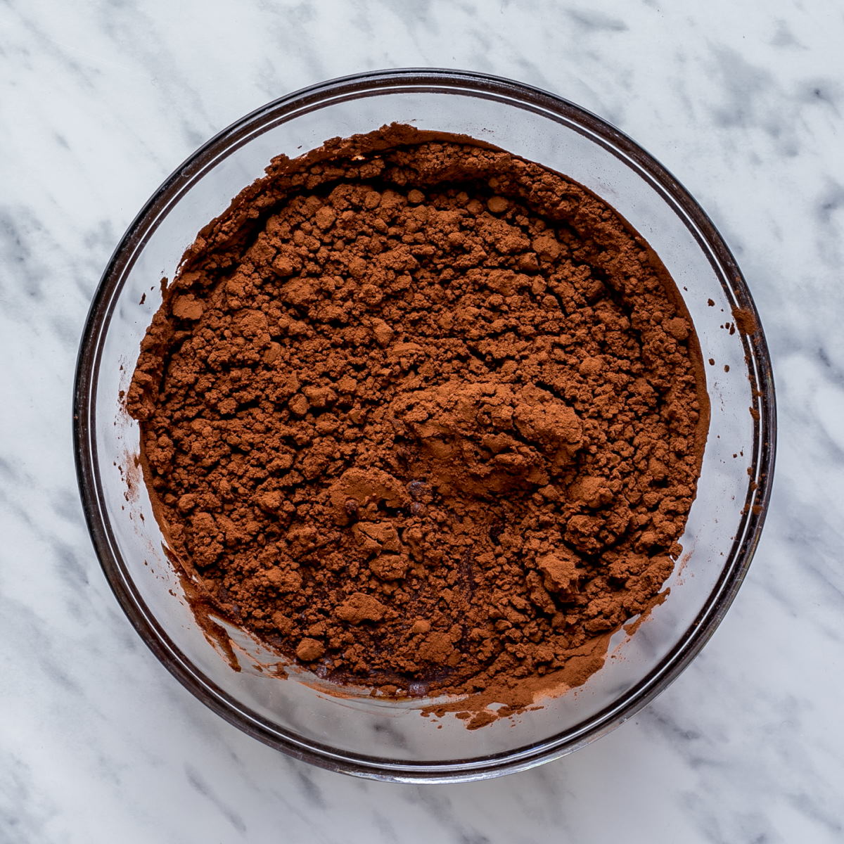 Cocoa powder on top of melted chocolate in a large glass bowl.