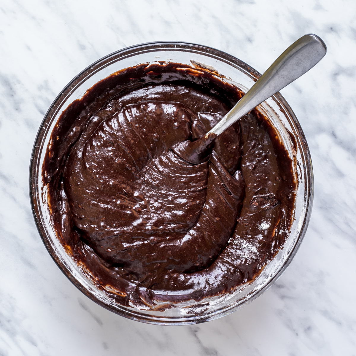 Gooey dark brown batter with a spoon in a glass bowl.