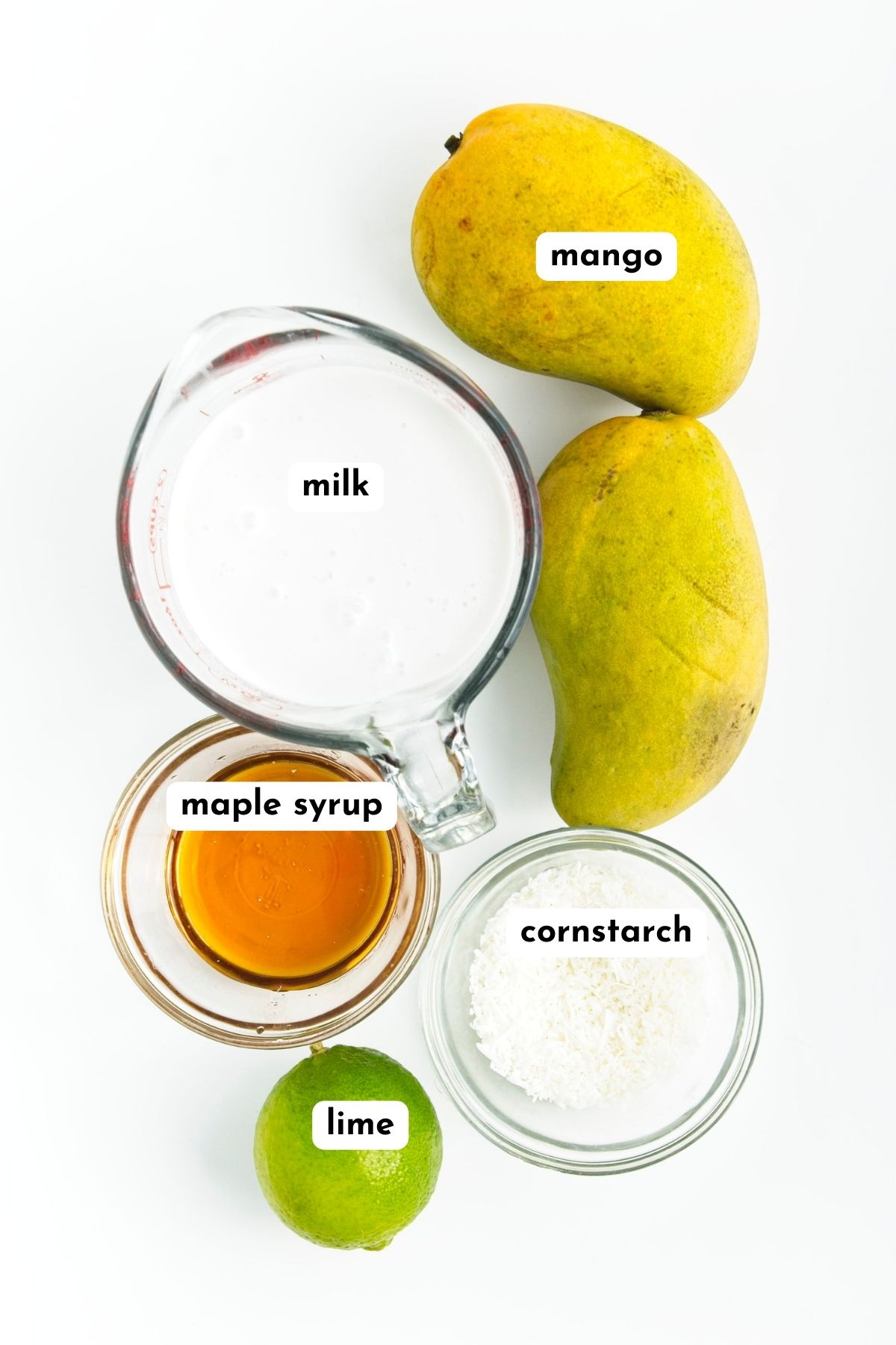 Ingredients of mango popsicles on a white surface like 2 large mangoes, coconut milk in jar, corn starch, maple syrup and lime. 