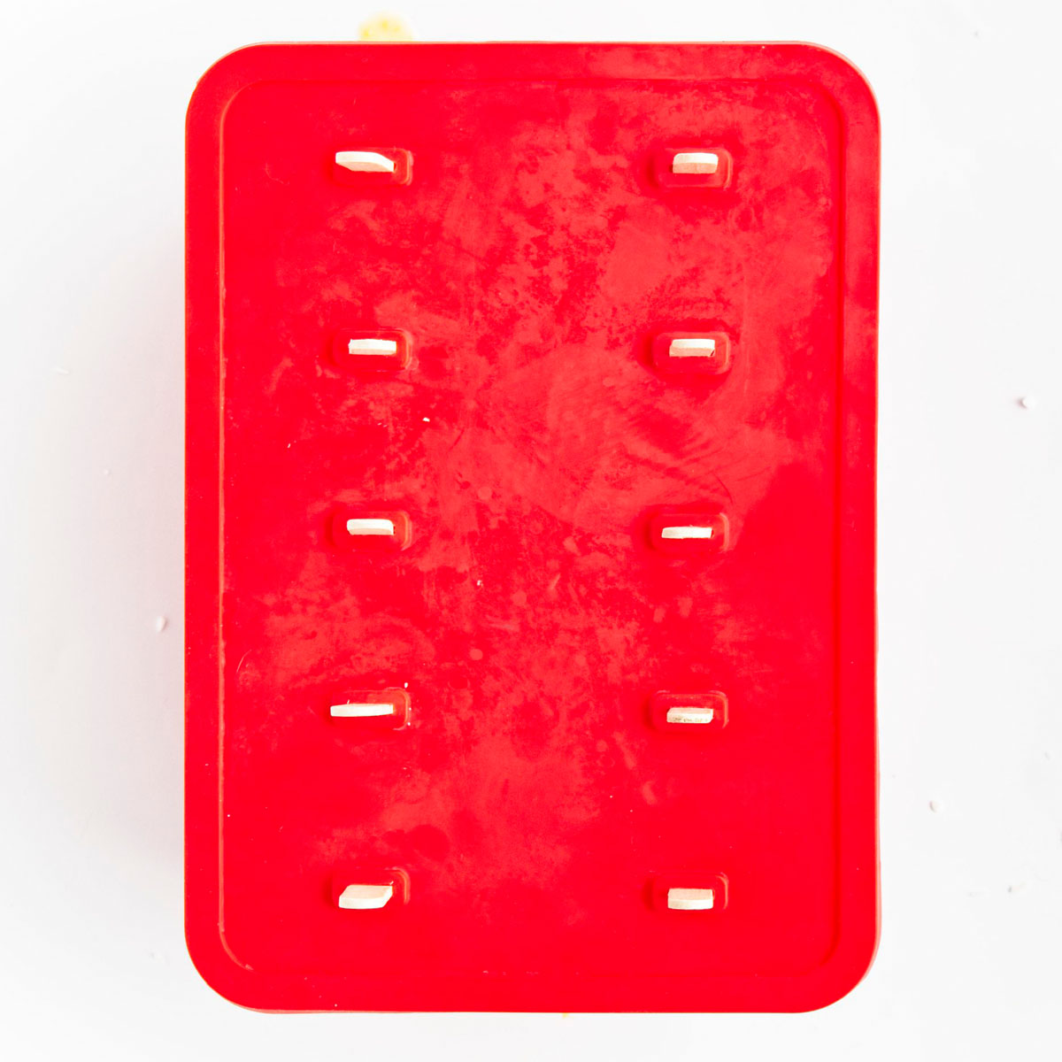 Red popsicle mold with the cover top on and 10 sticks are sticking out from it.
