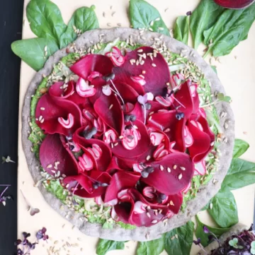 Salad in a form of a pizza with lots of vibrant purple beet slices.