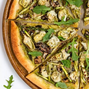 Pizza with green pesto, artichoke pieces, mushroom, and arugula.