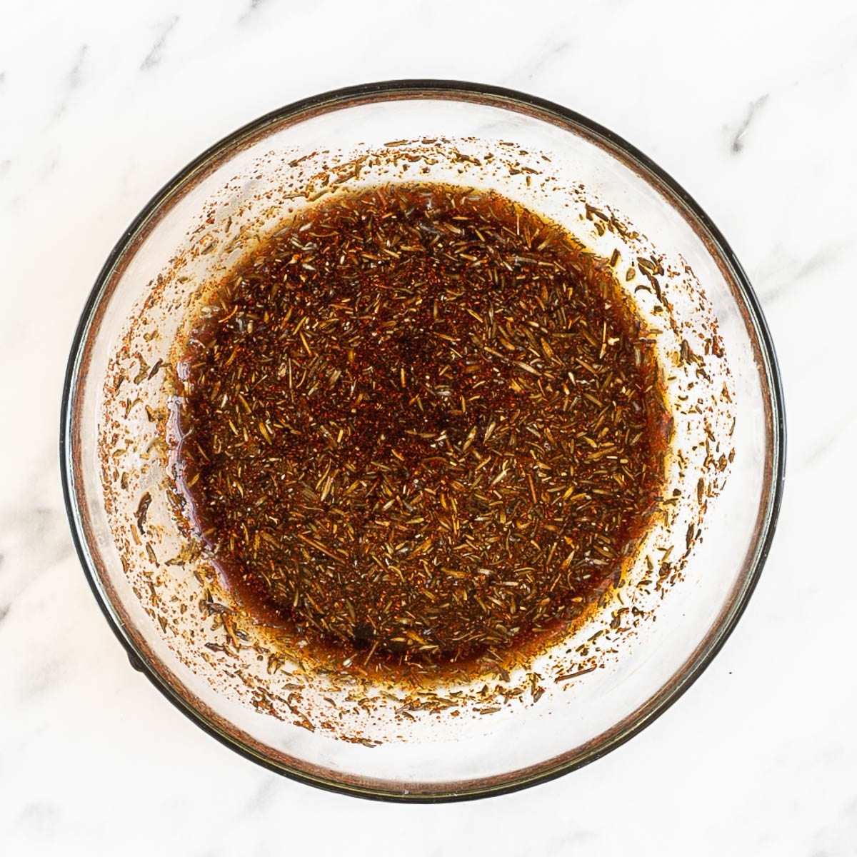 Dark sauce with spices and minced ginger and garlic in a glass bowl.