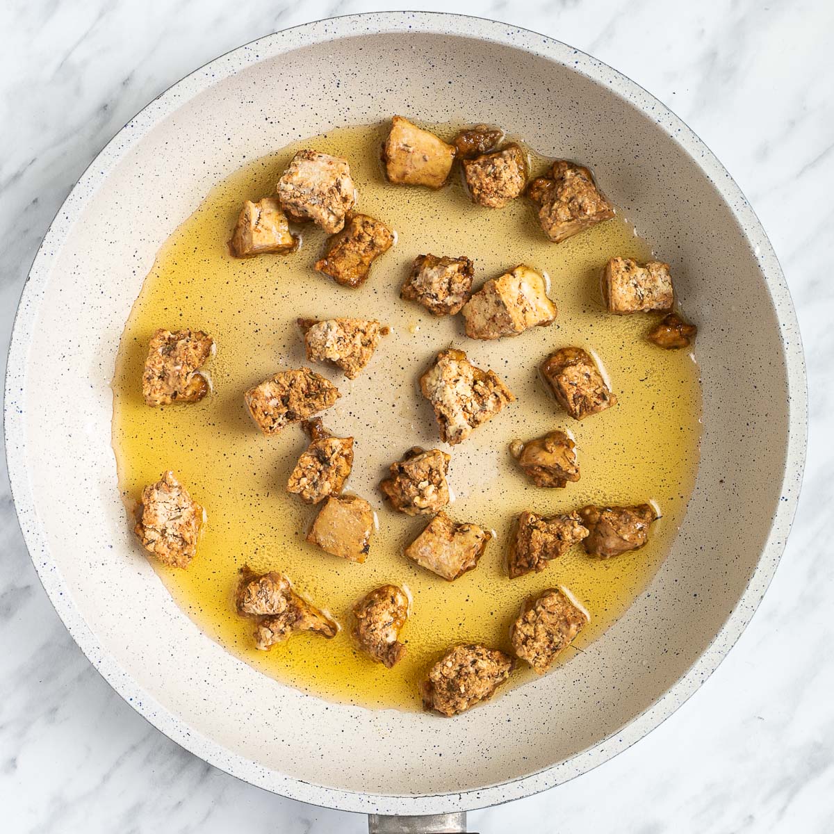 Light brown torn tofu pieces in a white frying pan.