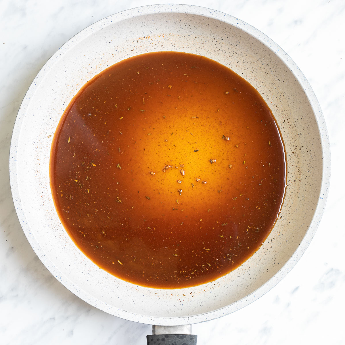 A white frying pan with different dark liquids and spices.