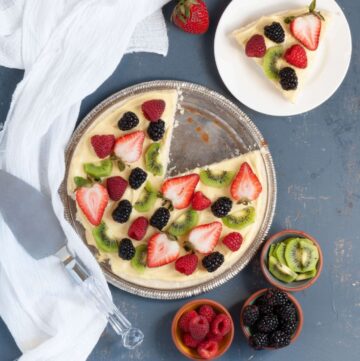 Large pizza-sized cookie topped with yellow sauce and lots of fresh fruit like strawberry, blueberry and grapes.