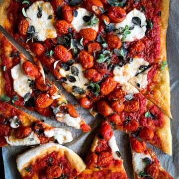 Pizza with red sauce, cherry tomatoes, melted vegan mozzarella, and fresh green herbs