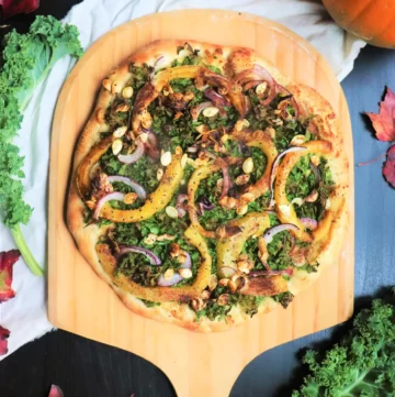 Pizza with lots of kale, roasted pumpkin slices, red onion slices, and roasted cashew nuts.