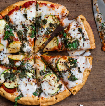 Pizza with red tomato sauce, zucchini slices, and liquid white melted mozzarella cheese. Sprinkled with chopped basil.