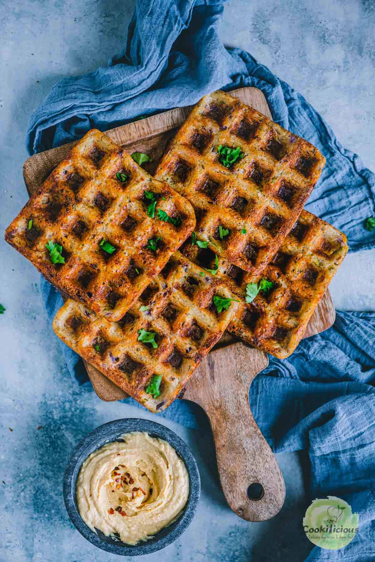 Crispy brown waffles on a wooden board sprinkled with chopped green herbs