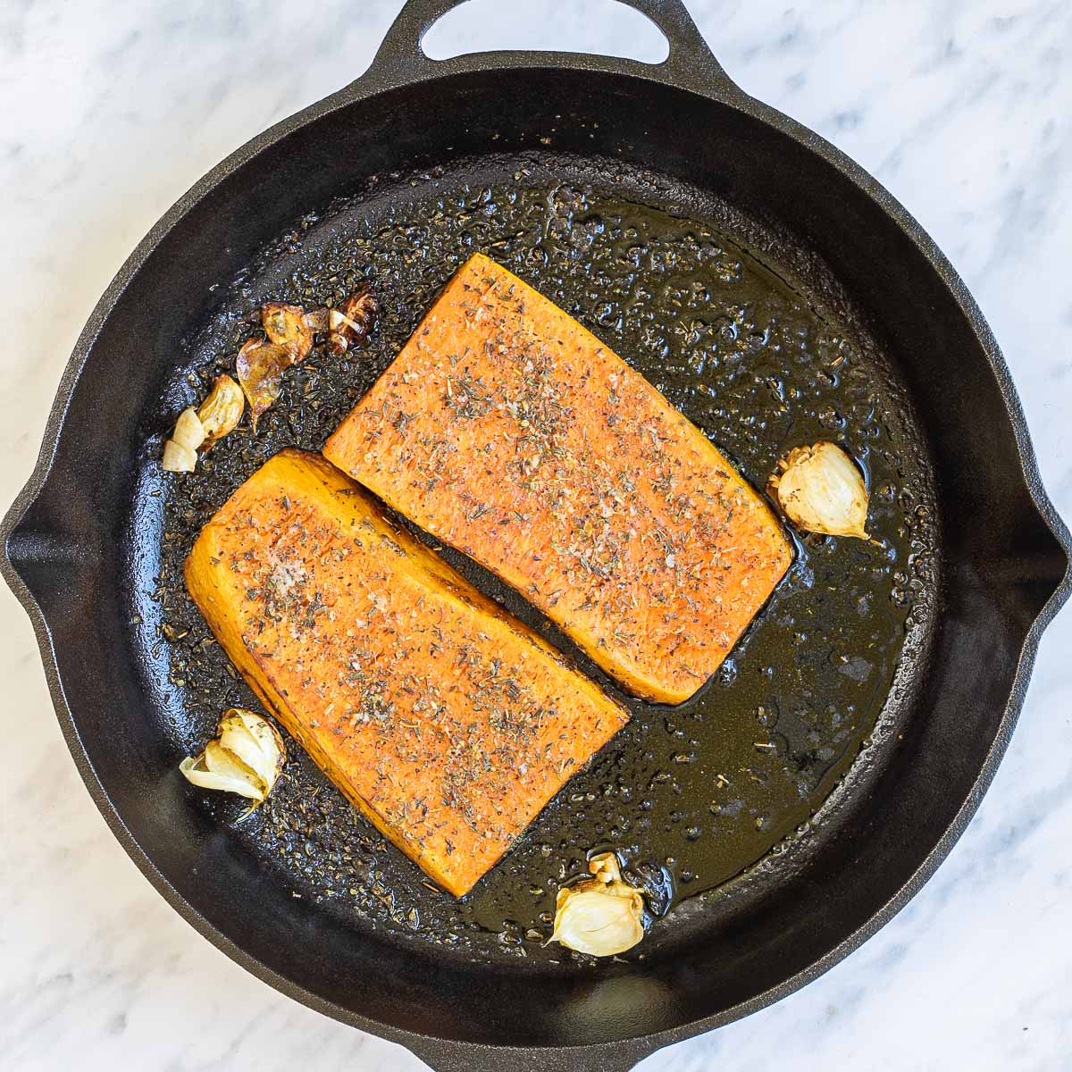 Cast iron skillet with two large squash slices and some garlic cloves in bubbling melted butter.