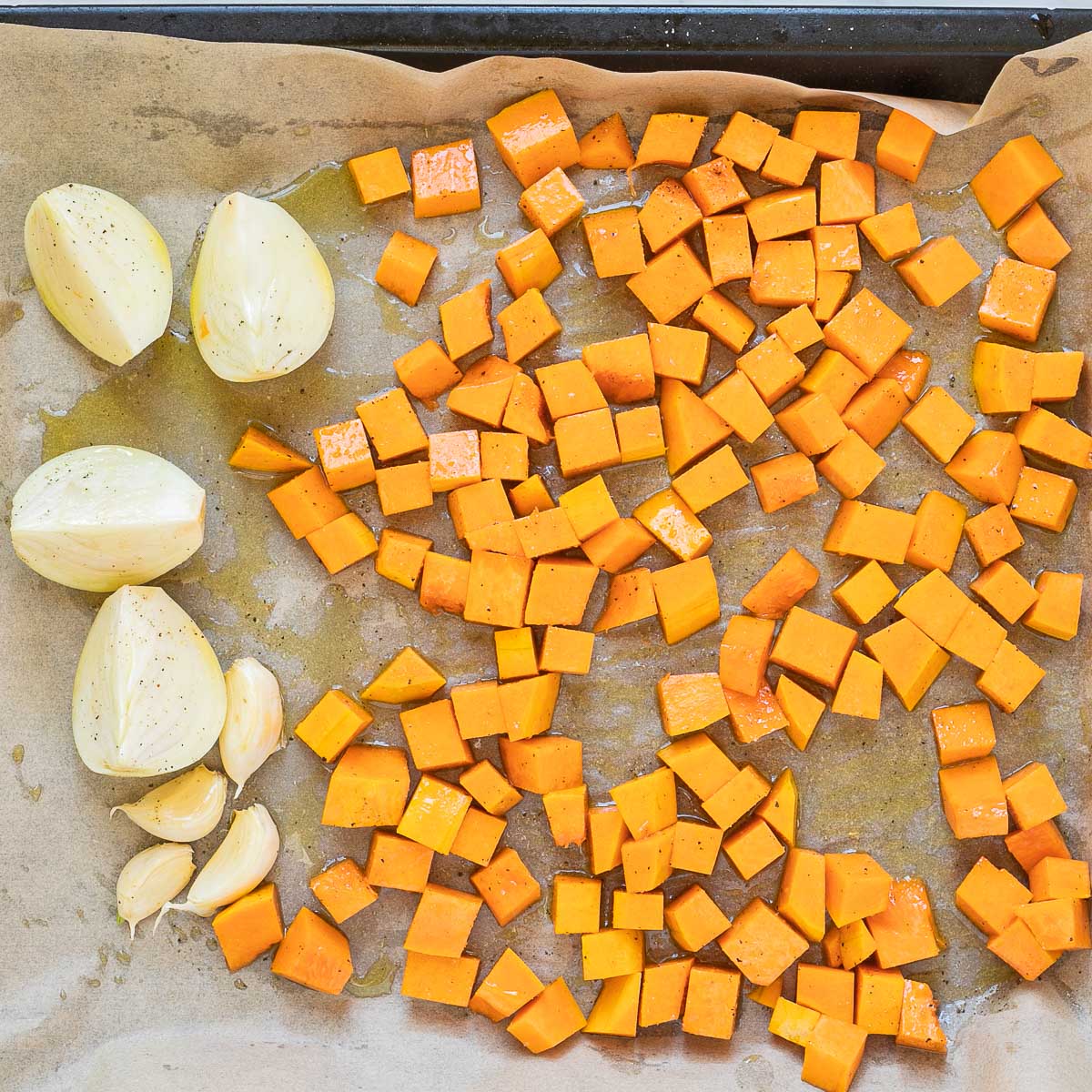 Sheet pan with orange squash cubes, white onion wedges and garlic cloves